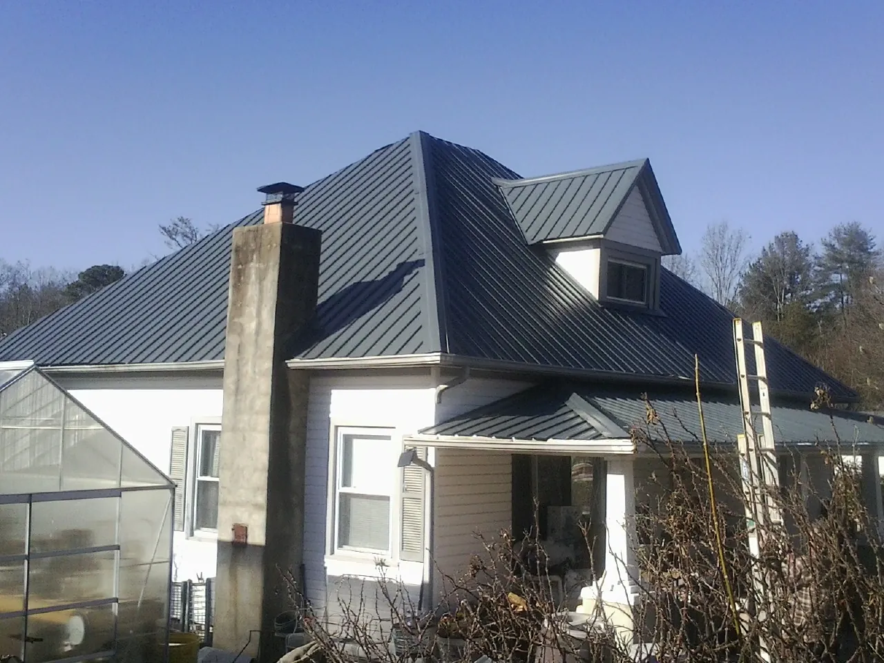Dark blue standing seam metal roof on a white farmhouse with dormer — Slate & Tile Roof Repair by Roofing Brothers in North Royalton