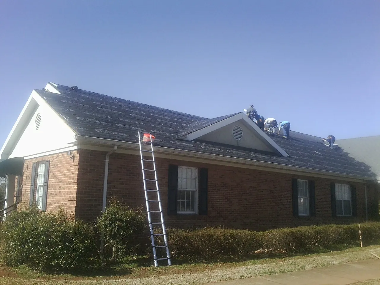 Crew tearing shingles off a brick ranch roof with a ladder set — Emergency Roof Repair work by our crew in North Royalton