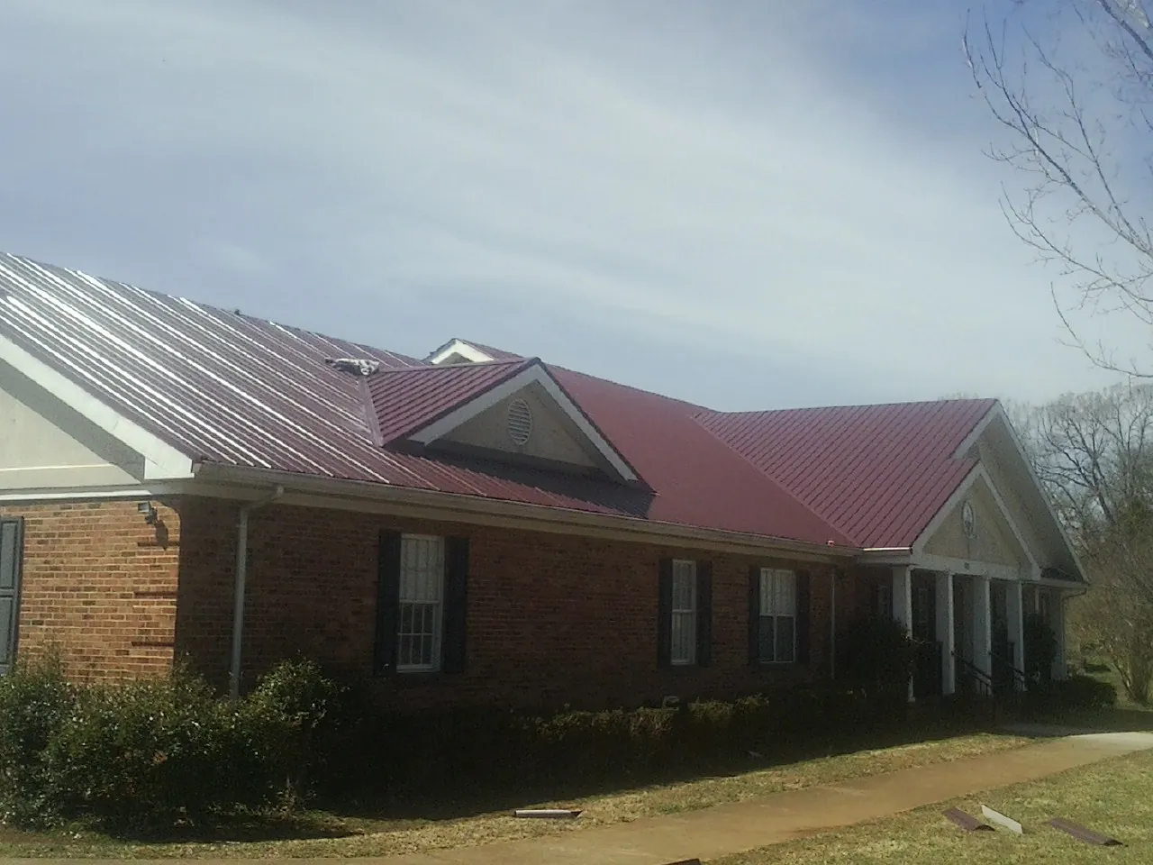 Red metal roof with gabled entries on a long brick building, from a Hail Damage Roof Repair job in North Royalton