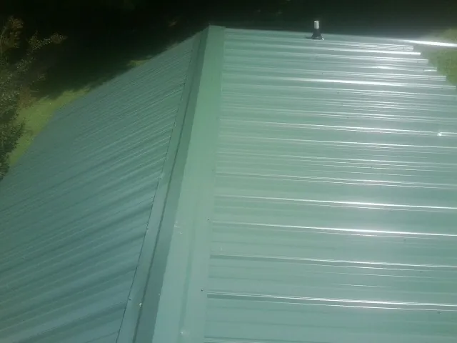 New green metal panels meeting at the ridge of a roof — Flat Roof Repair work by our crew in North Royalton
