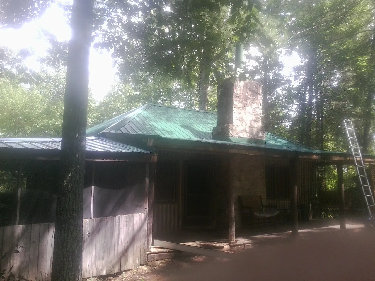 Green metal roof and stone chimney above a log cabin porch in North Royalton
