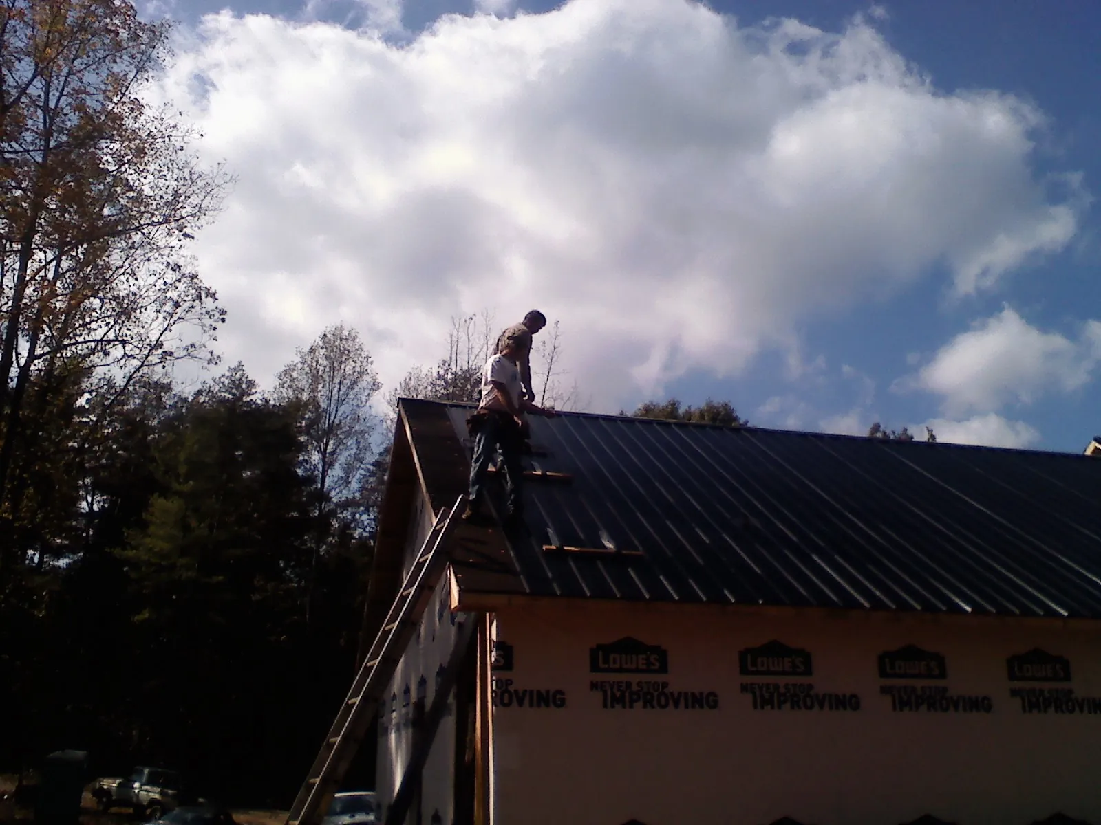 Roofer fastening dark metal panels high against a cloudy sky, from a Roof Inspection job in North Royalton