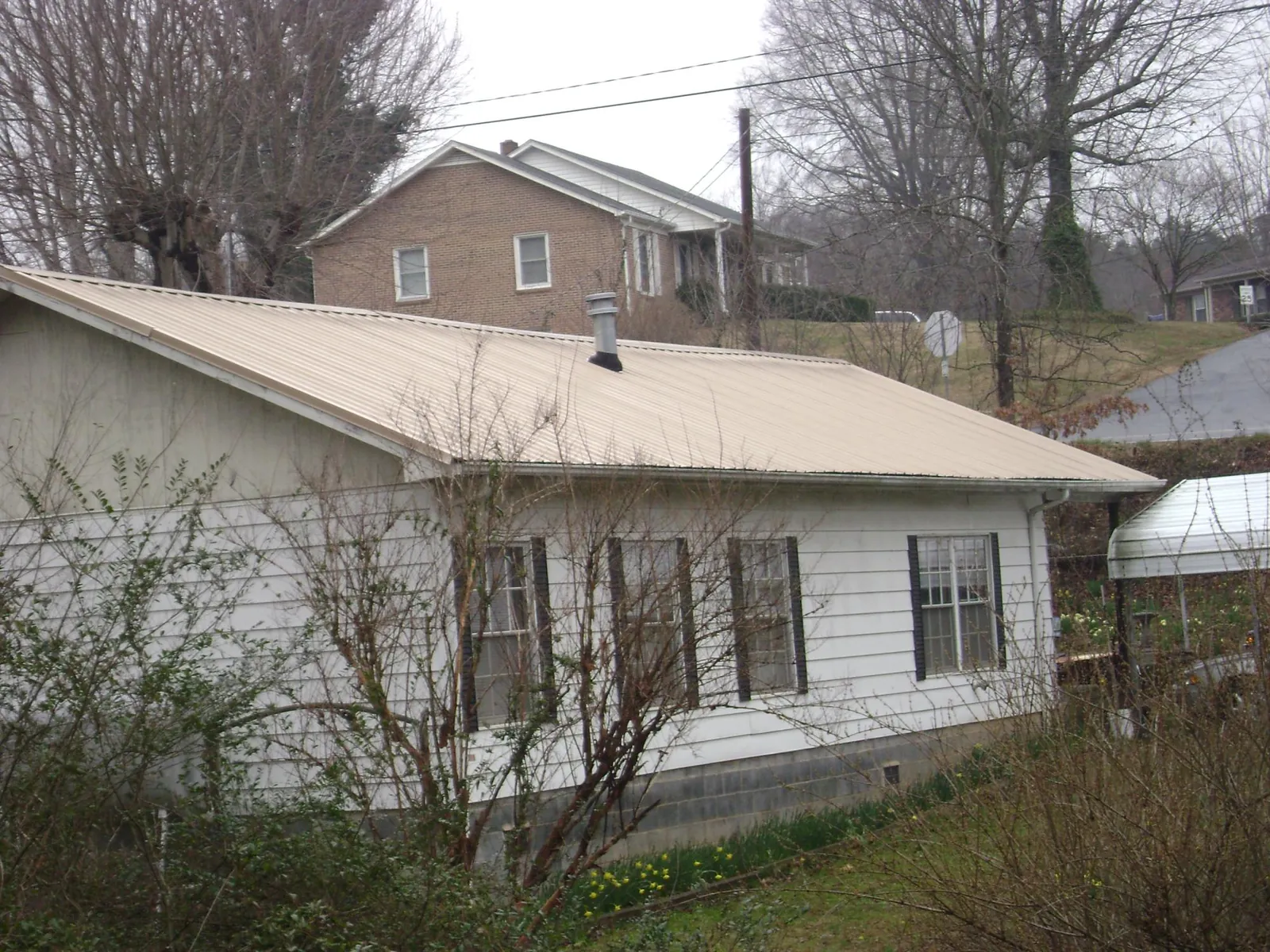 Tan metal roof on a white sided house set into a hillside — Commercial Roofing by Roofing Brothers in North Royalton